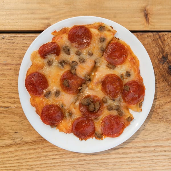 Pepperoni and sausage pizza on a white plate, viewed from above on a wooden table.