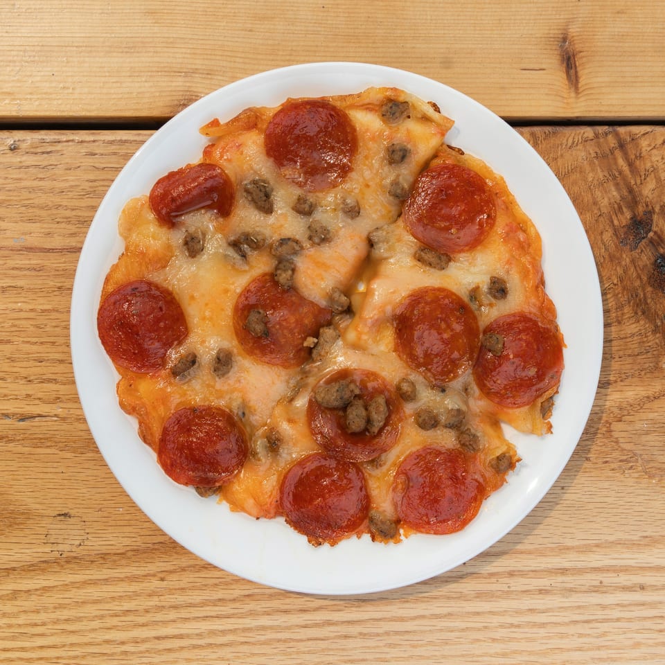 Pepperoni and sausage pizza on a white plate, viewed from above on a wooden table.