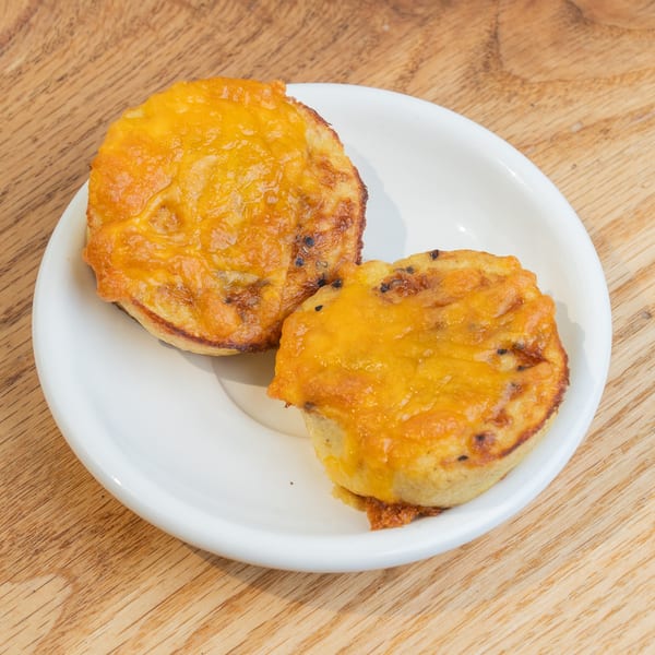 Two golden-brown savory muffins topped with melted cheese on a white plate.
