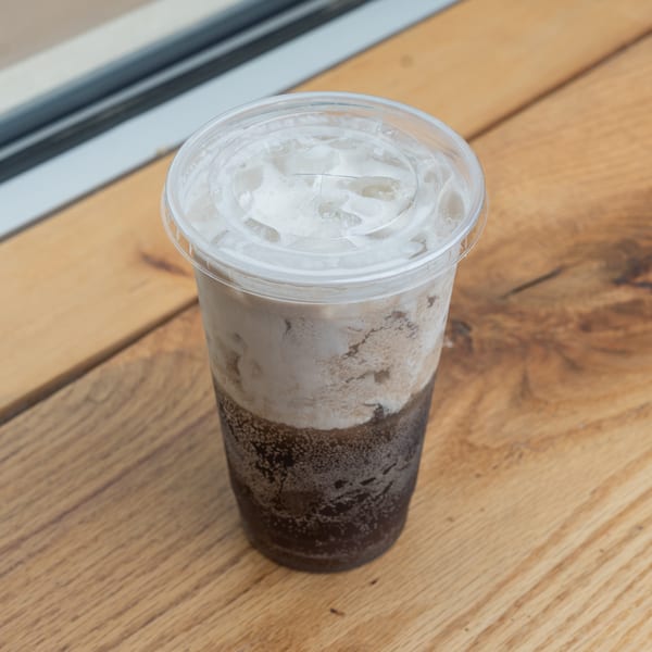 Iced coffee drink with creamy top layer in a plastic cup on a wooden table.