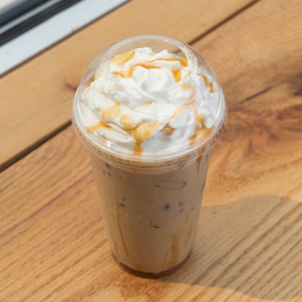 Iced coffee with whipped cream and caramel drizzle in a plastic cup on a wooden table.