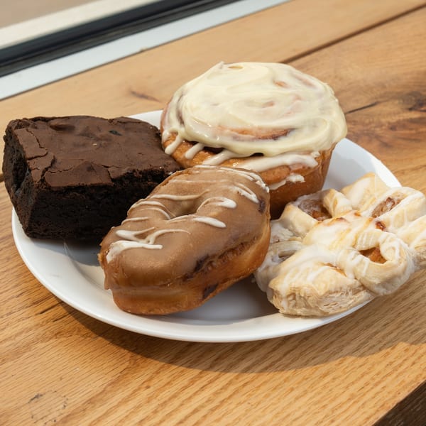 Assorted pastries including a brownie, cinnamon roll, donut, and danish on a white plate.