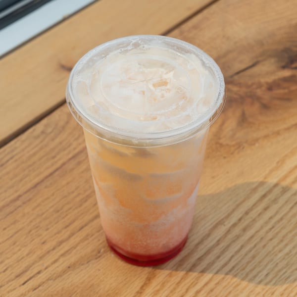 Refreshing layered orange and red iced drink in a plastic cup on a wooden table.