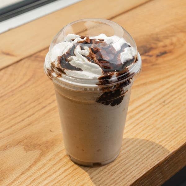Blended coffee drink with whipped cream and chocolate drizzle in a clear cup on wood.