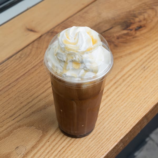 Iced coffee with whipped cream and a golden drizzle in a plastic cup on a wooden surface.