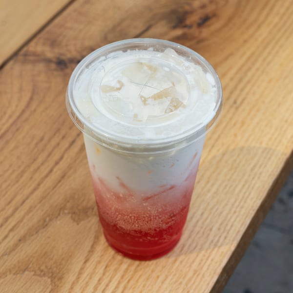Bubbly red and creamy white layered drink in a plastic cup on a wooden surface.